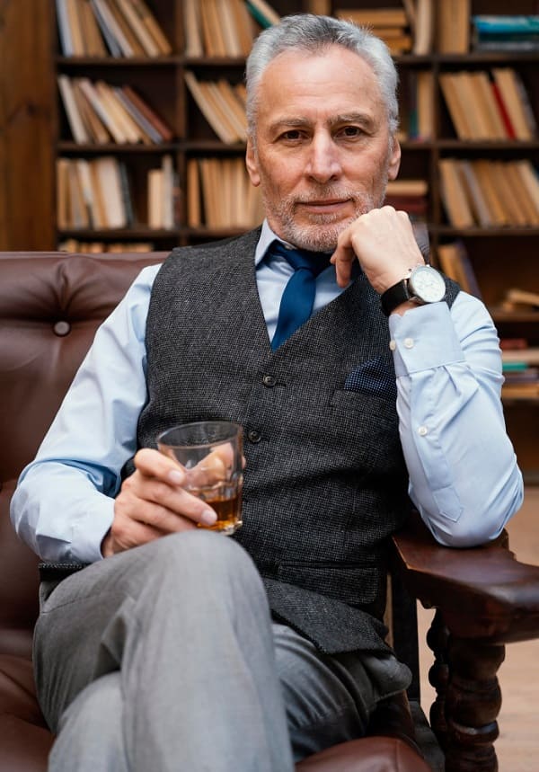 Um homem de meia-idade bem-sucedido está sentado no sofá com uma taça de vinho pela metade.